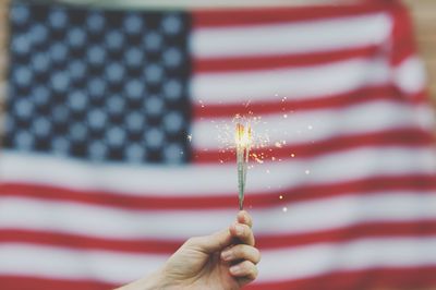 Cropped hand holding illuminated sparkler against american flag