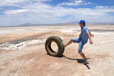 Man pushing tire while standing on sand at desert