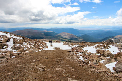 Mid distant view of hikers walking on mountain against sky during winter