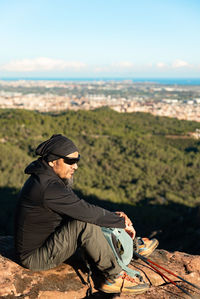 Side view of woman sitting on rock against sky