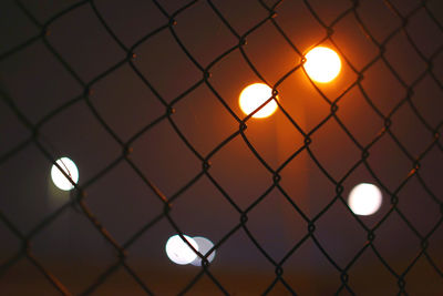 Close-up of illuminated chainlink fence at sunset