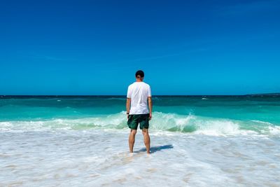 Rear view of man standing at beach against sky