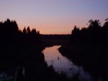 Silhouette trees by lake against sky at sunset