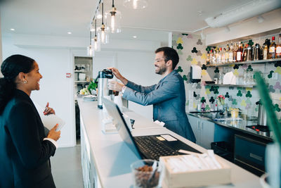 Smiling owner making coffee for female customer at office cafeteria