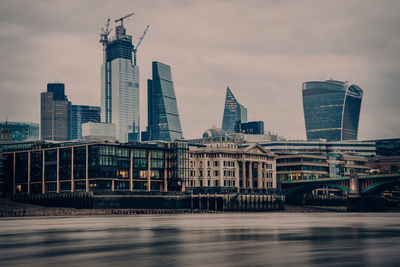 Bridge over river by buildings against sky in city