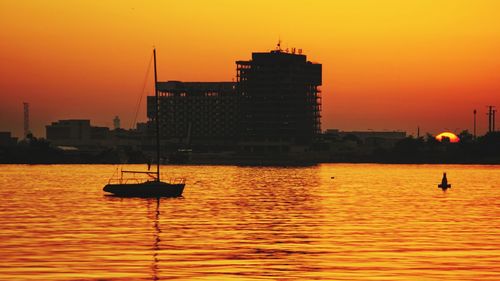 Silhouette sailboats in sea against orange sky