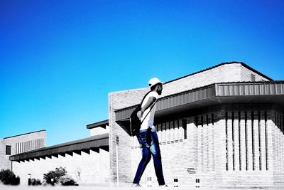 Low angle view of person against building against clear blue sky