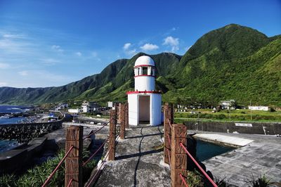 Lighthouse by mountain against blue sky