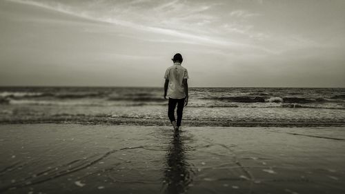 Rear view of man standing on beach against sky