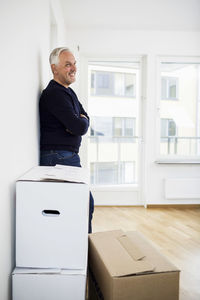 Side view of mature man standing by moving boxes at home