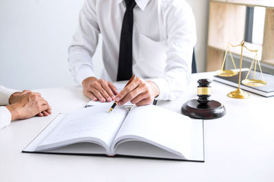 Midsection of judge writing on book while client sitting at table