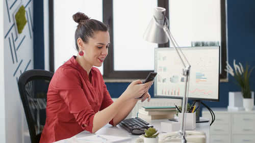 Smiling businesswoman using phone sitting at home