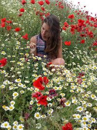 Young woman sitting amidst white daisies and red poppies blooming on field