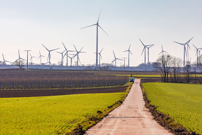 A multitude of wind turbines cluster on the horizon behind agricultural fields in germany