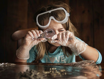 Girl looking at object through magnifying glass while sitting at table