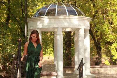 Portrait of smiling woman in green silk dress standing against autumn park