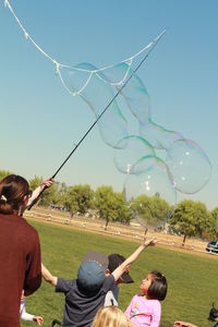Children playing with bubbles in park against sky