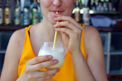 Midsection of woman drinking drink through straw at restaurant
