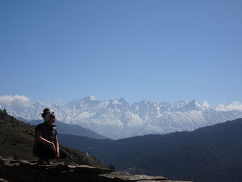 Man sitting on mountain against sky