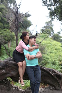 Beautiful woman embracing man while sitting on fallen tree