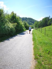 Woman with dog walking on road against sky