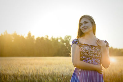 Young woman standing on field against sky