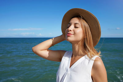 Smiling girl with hat breathing fresh air with blue sea on the background