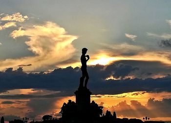 Silhouette of statue against cloudy sky during sunset