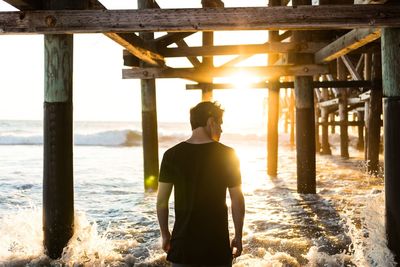 Rear view of man standing below pier at beach