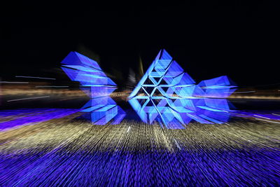 Illuminated ferris wheel against blue sky at night