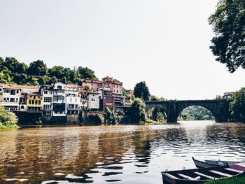 Arch bridge over river by buildings against clear sky