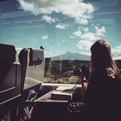 Woman with camera sitting in train while looking at mountain