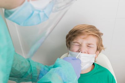 Side view of medic in protective uniform conducting pcr test on covid virus while taking nasal swab from kid