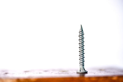 Close-up of screw on wooden table against white background