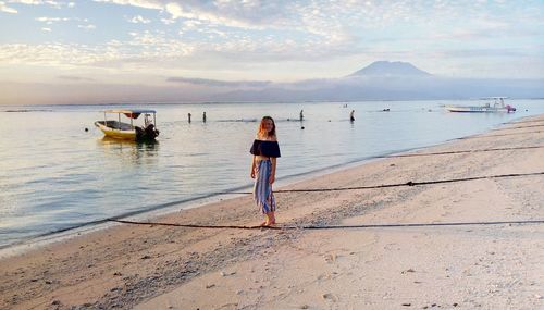 Woman standing on shore at beach against sky