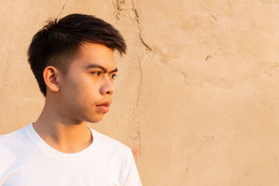 Portrait of young man looking away against wall