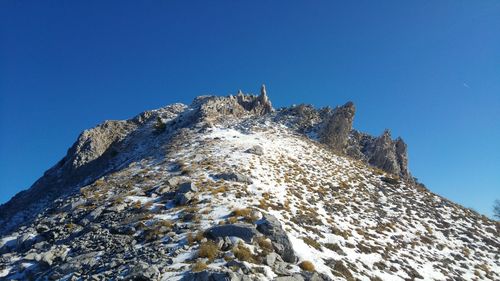 Low angle view of rocky mountain against clear blue sky