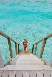 High angle view of mid adult bikini woman walking on steps in sea