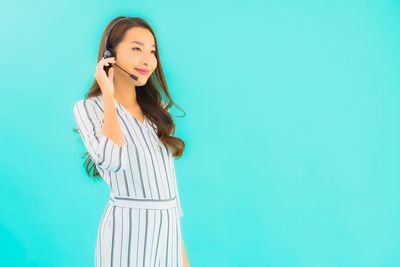 Young woman looking away while standing against blue background