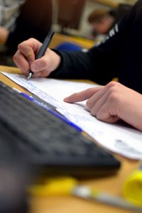 Cropped image of person writing in notebook by computer keyboard at school