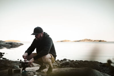 Full length of man cooking food on camping stove at lakeshore during sunset