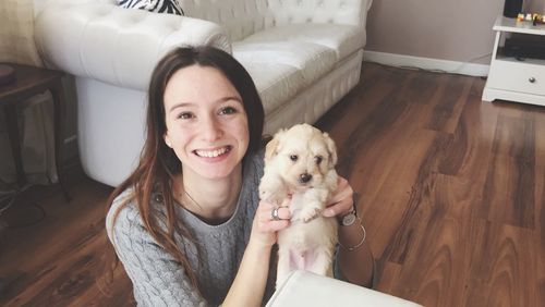 Portrait of woman holding puppy while sitting on floor at home