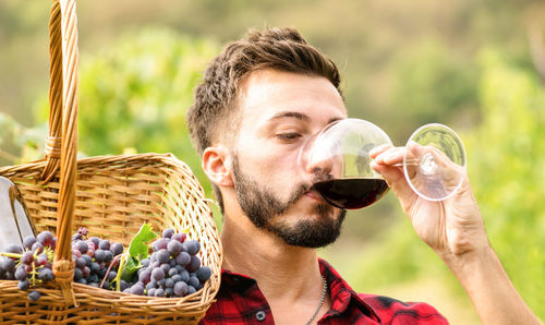 Close-up of man drinking wine while holding in basket at vineyard