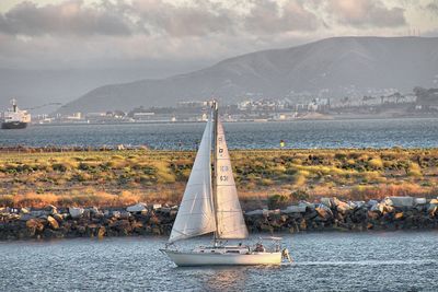 Boat sailing on sea by mountains against sky