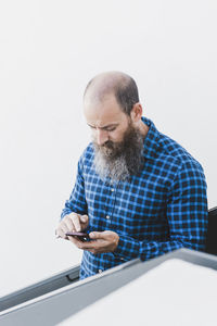 Busy male worker standing in creative workspace and browsing cellphone while working on new project