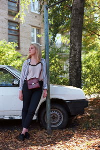 Full length of woman standing by car against trees