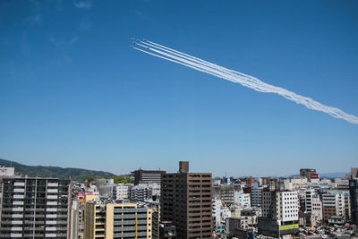 Aerial view of vapor trail in city against clear blue sky