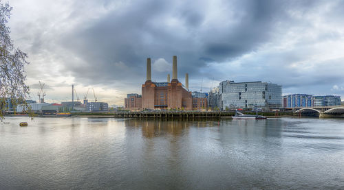 Buildings by river against cloudy sky