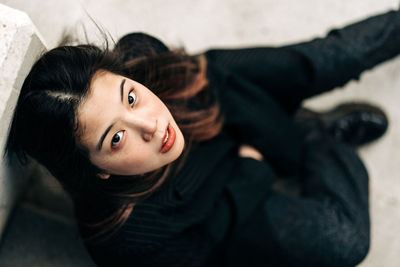 Long hair brunette asian woman sitting on some stairs and looking at camera