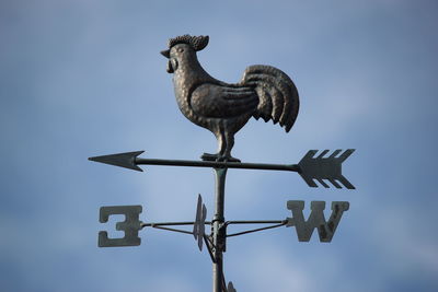 Low angle view of rooster sculpture on weather vein against sky